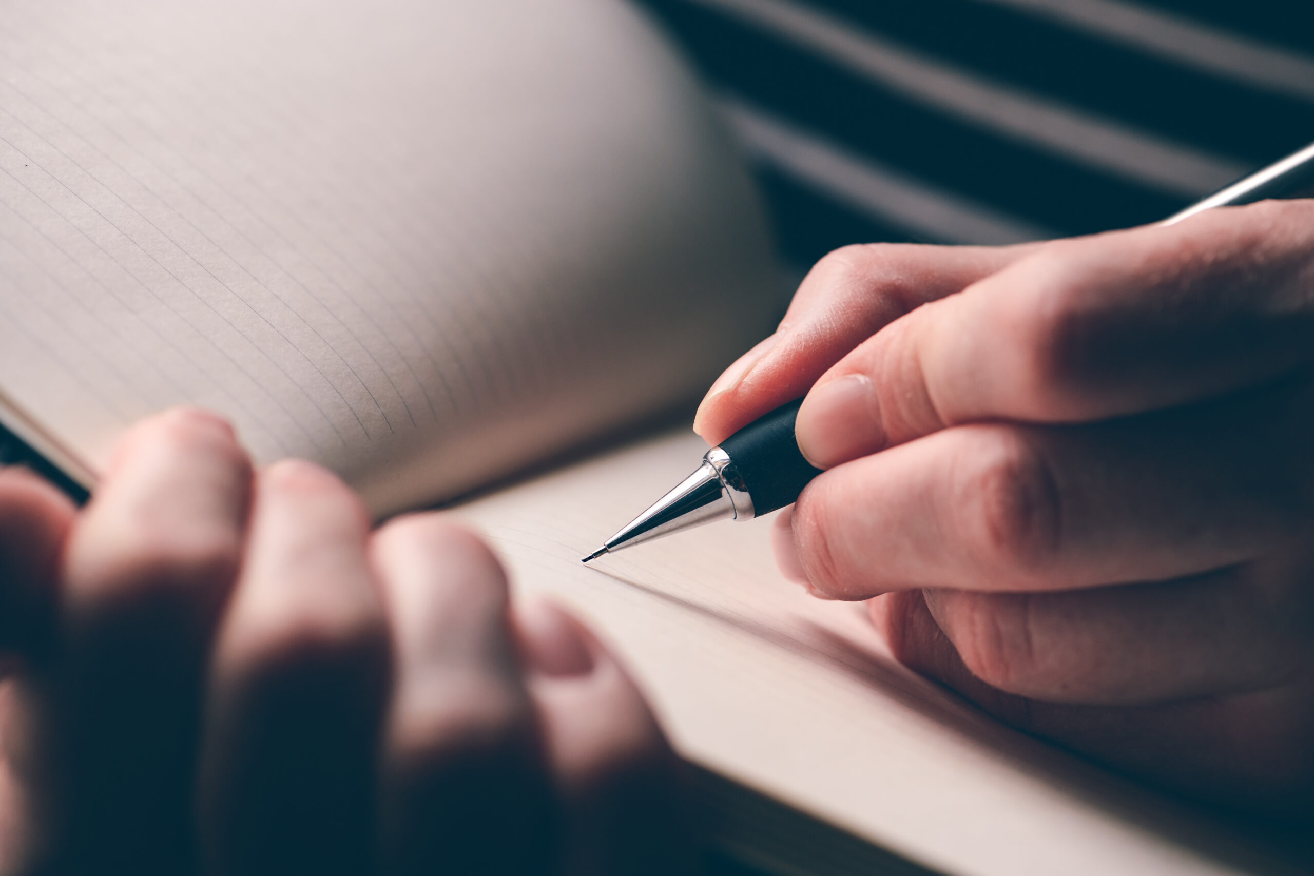 Hand poised with a pen above a blank lined notebook page, focusing on the writing process, emphasizing creativity and thought.